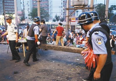 6月13日晚8點，朝陽路和青年路交叉口西側(cè)，一次聯(lián)合執(zhí)法行動中，輔警與協(xié)管抬走商戶的燒烤用具。新京報記者 尹亞飛 攝