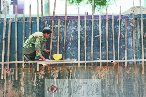 　　烈日下，狹窄的架子上，工人正用錘子固定樁基。