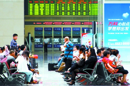 候車大廳溫度很高，一名乘客一手扇風(fēng)、一手擦汗