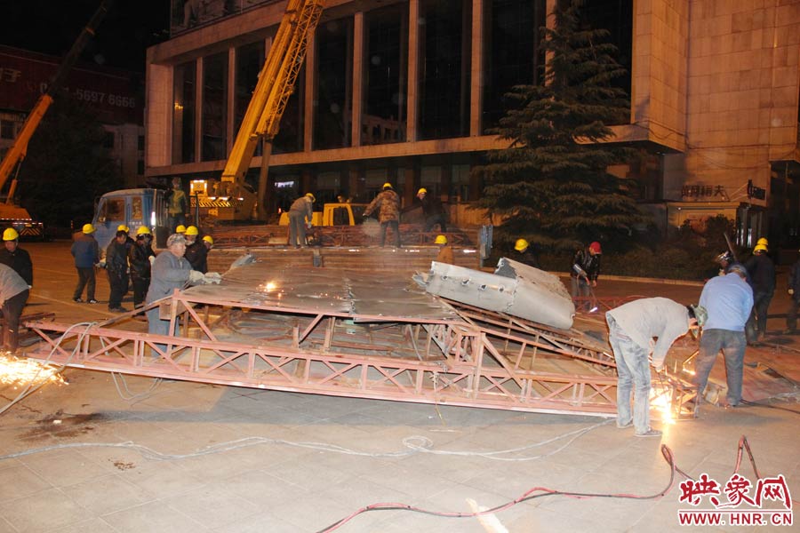 地面上的20多名工人對吊裝下的廣告牌進(jìn)行分割。