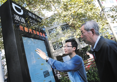 10月15日，滴滴工作人員（左）指導(dǎo)乘客使用“滴滴車站”的電子屏預(yù)約出租車。