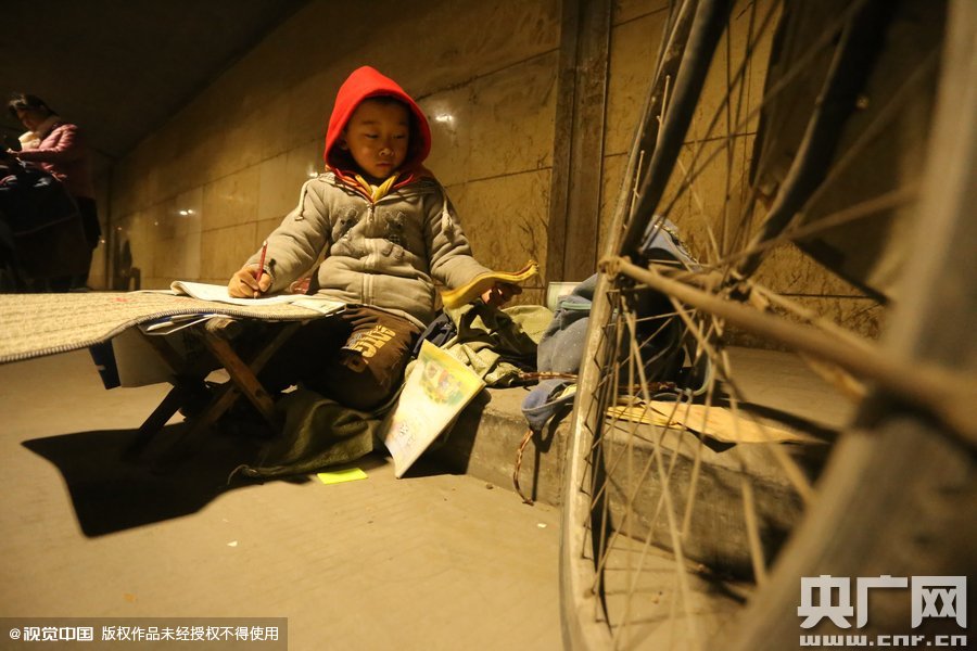 2015年11月8日晚，鄭州，7歲男孩涵洞橋下陪父母練攤，路邊燈下坐小馬扎上寫作業(yè)。