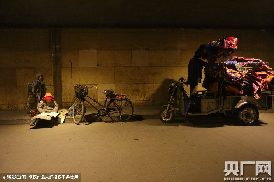 2015年11月8日晚，鄭州，7歲男孩涵洞橋下陪父母練攤，路邊燈下坐小馬扎上寫作業(yè)。