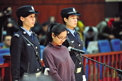 被告人盧梅低著頭，站在朝陽法院刑事審判庭的被告席上。