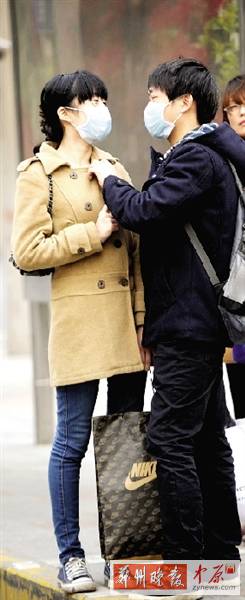 公交站臺(tái)上，一對(duì)年輕人戴著口罩，系緊衣領(lǐng)。